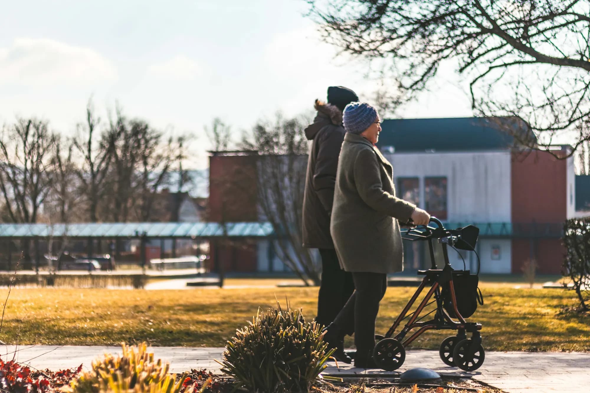 Eine ältere Frau mit Rollator und eine Begleitperson bei einem Spaziergang