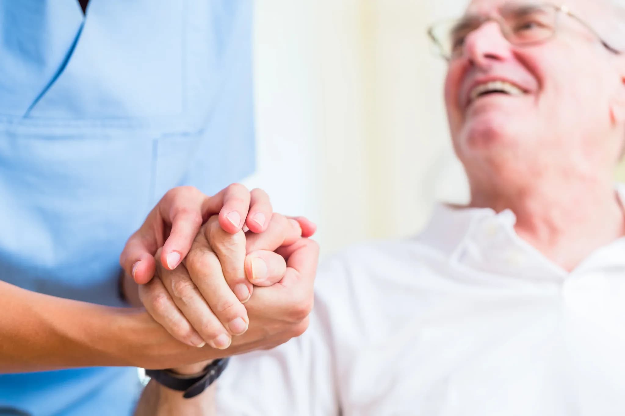 Pflegekraft hält die Hand eines lachenden älteren Mannes