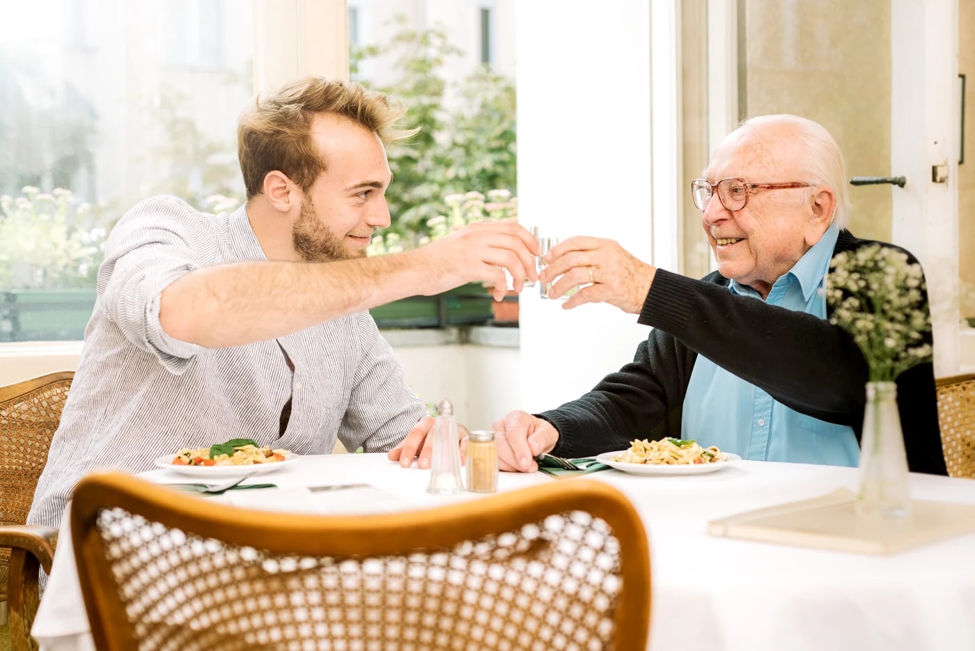 Ein Alltagsbegleiter und ein älterer Mann sitzen gemeinsam beim Mittagessen.