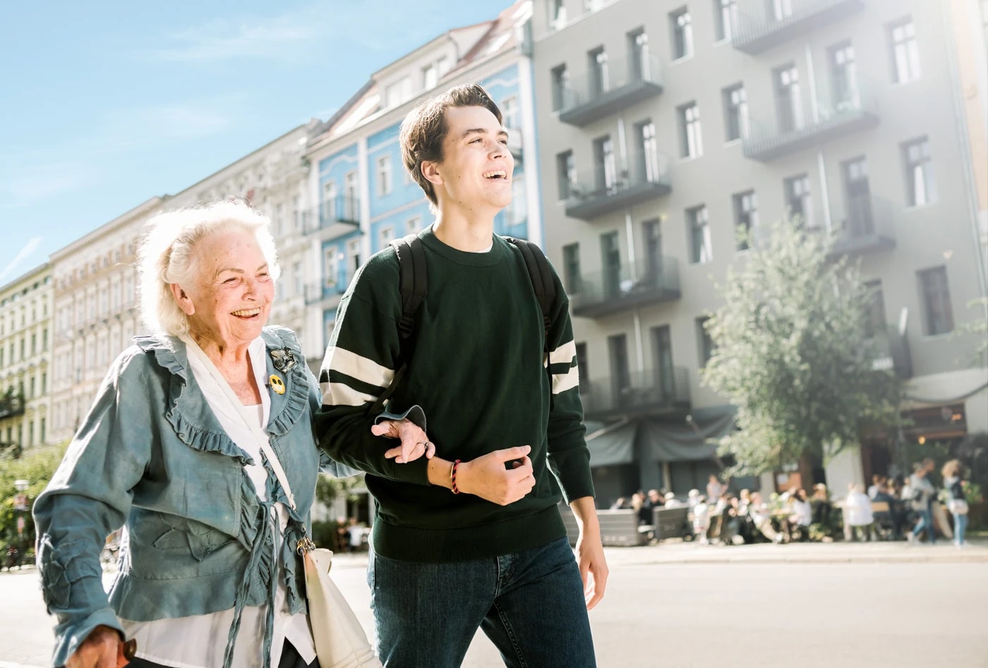 Ein Alltagshelfer begleitet eine Seniorin mit Einkaufstasche durch die Stadt.