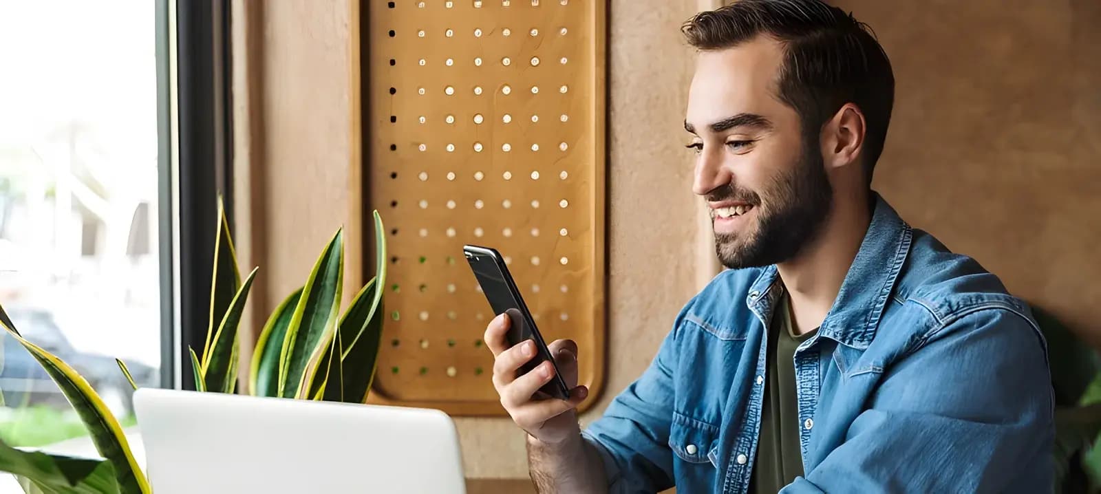 Ein Mann nutzt ein Smartphone an seinem Arbeitsplatz mit Laptop